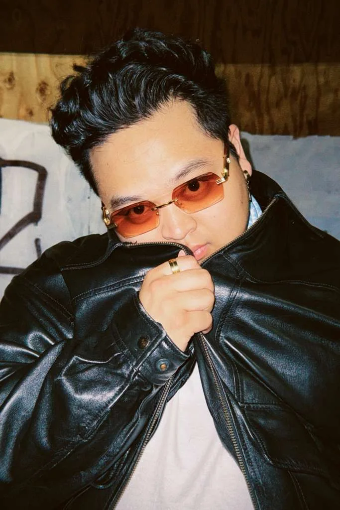 Justin Magnaye wearing amber glasses and a black leather jacket at night.